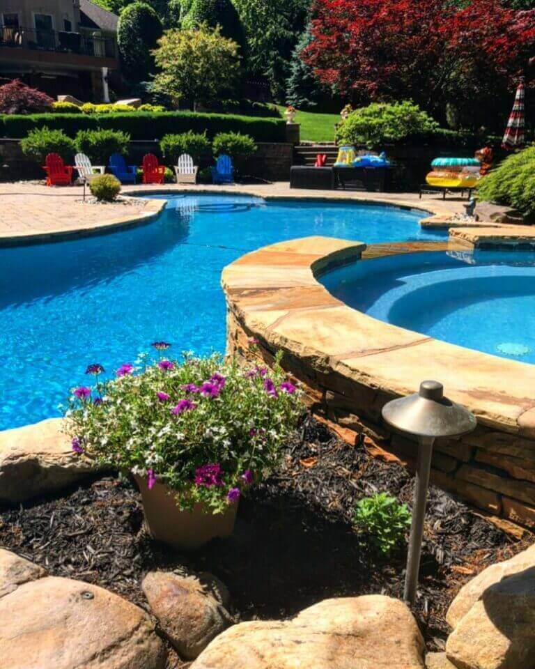 Pool with stone waterfall and coping surrounded by plantings