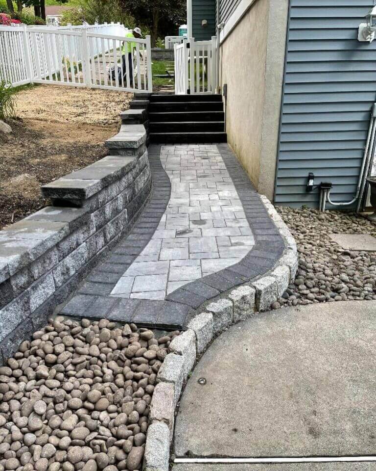 New paver walkway with river rock border beside a house