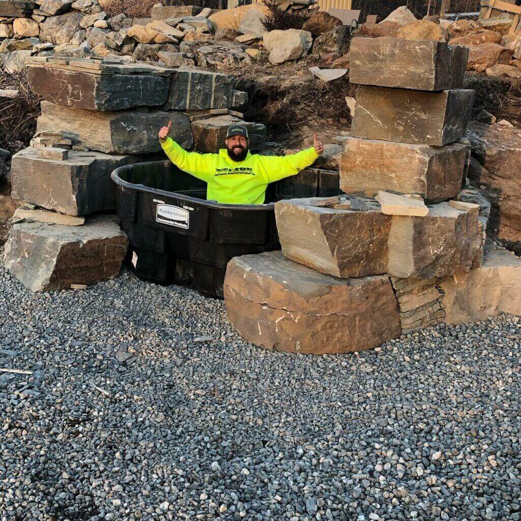 Worker placing large boulder wall stones on gravel base