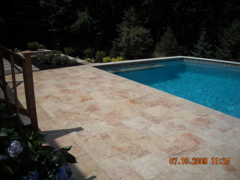 Travertine pool patio with glass railing beside an in-ground pool